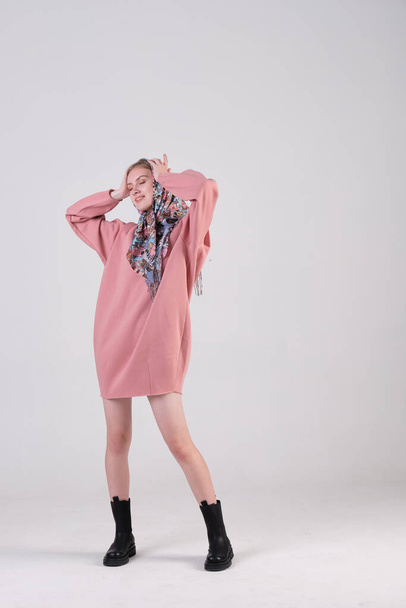 Russian young fashion model wearing ethnic shawl on her head and pink oversized dress posing in studio cyclorama. - Фото, зображення