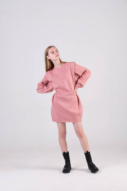 young fashion model wearing   pink oversized dress and black boots posing in studio cyclorama. Concept of clothes advertisement. - Photo, image
