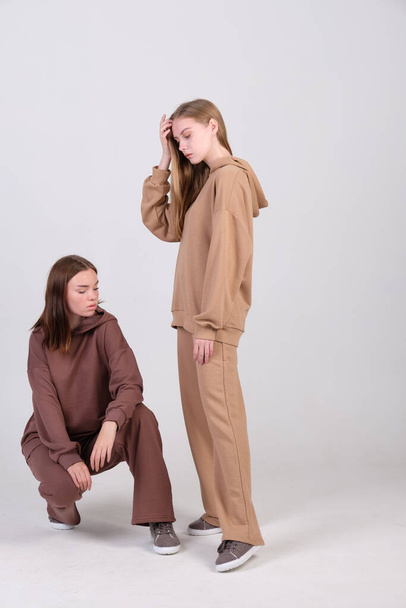 Pair of fashionable models posing in studio in brown and beige casual suits for clothing catalog. Examples of autumn female fashion. Copy space. - Foto, afbeelding