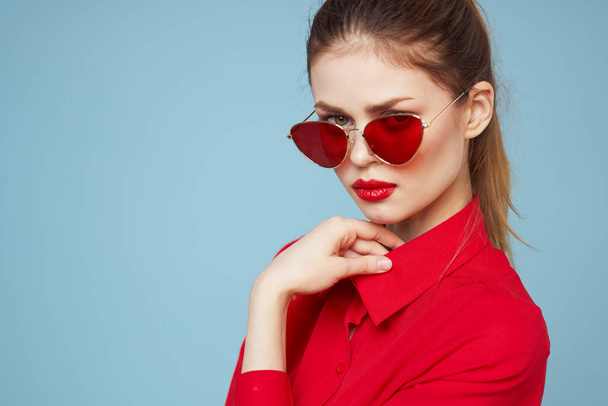 Beautiful woman in dark glasses red shirt bright makeup emotions attractive look blue background - Foto, Imagen