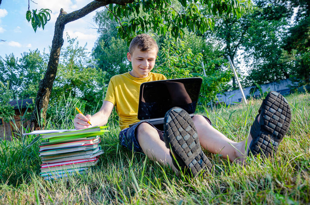 Le gars est un étudiant, un écolier est fiancé, faisant des leçons en ligne dans le jardin sous l'arbre. - Photo, image