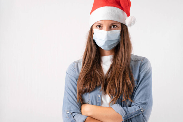 Young woman with medical mask and santa hat on white background. Christmas on quarantine. - Photo, image