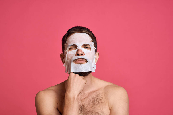 Man with bare shoulders in a white mask clear skin pink background - Foto, afbeelding