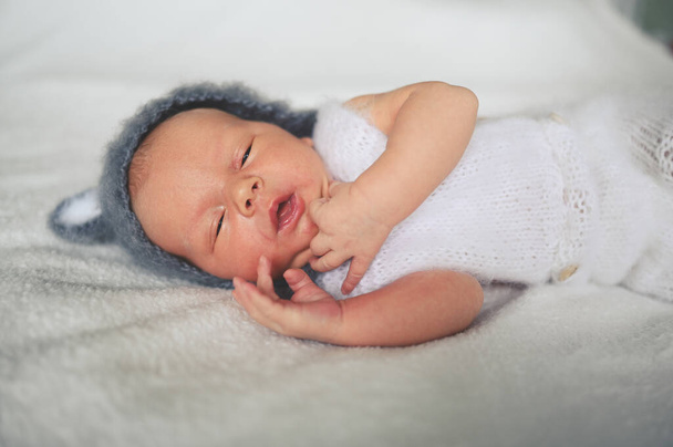 Χαριτωμένο συναισθηματικό νεογέννητο αγοράκι που κοιμάται σε κούνια με πλεκτό κοστούμι και αυτιά. Πρότυπο συσκευασίας ειδών μωρών. Υγιές παιδί, έννοια του νοσοκομείου και ευτυχισμένη μητρότητα. Βρέφος. Φυτώριο. - Φωτογραφία, εικόνα