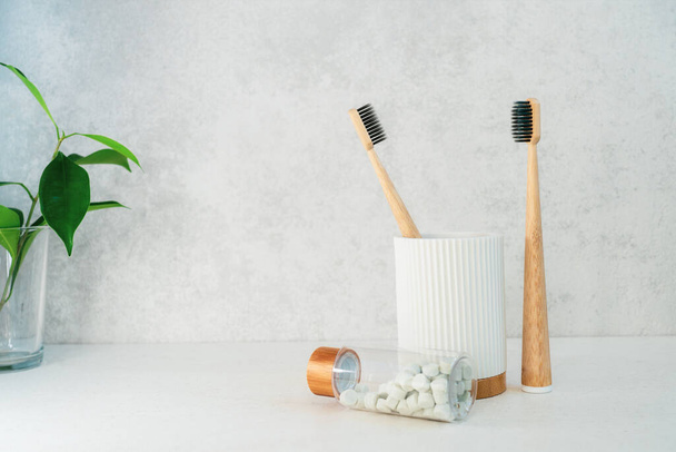 Zero waste bathroom items. Bamboo toothbrushes in recycling material holder, natural mouthwashing tabs and fresh green plants in glass. Oral care essentials. Eco-friendly home. Minimalism. Copy space. - Fotó, kép