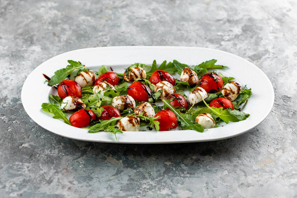 Świeża włoska sałatka z pomidorami, serem mozzarella i peso podawane na białym talerzu na zielonym, brudnym stole - Zdjęcie, obraz