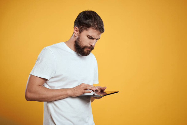 Man met een tablet op een gele achtergrond in een wit t-shirt nieuwe technologieën zakenman touch screen touchpad - Foto, afbeelding