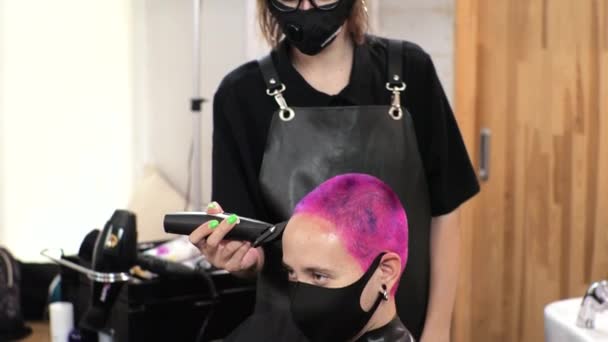 Parrucchiere taglia i capelli corti con un clipper Salone di casa durante l'epidemia con una maschera sul viso. - Filmati, video