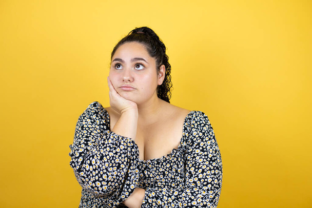 Jonge mooie vrouw met krullend haar over geïsoleerde gele achtergrond denken kijken moe en verveeld met gekruiste armen - Foto, afbeelding