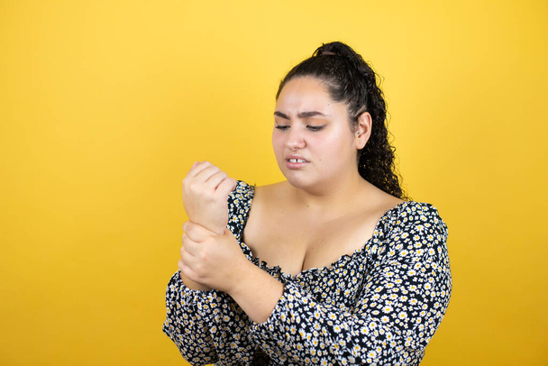 Jonge mooie vrouw met krullend haar over geïsoleerde gele achtergrond lijden pijn op handen en vingers, artritis ontsteking - Foto, afbeelding