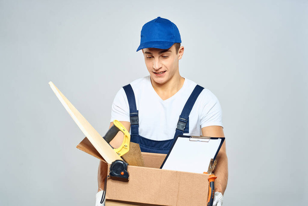 человек в рабочей форме с коробкой в руках инструменты погрузчика доставки легкий фон - Фото, изображение