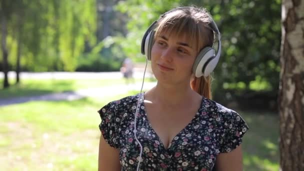 Mujer caminando en el parque con auriculares y escuchando música - Imágenes, Vídeo