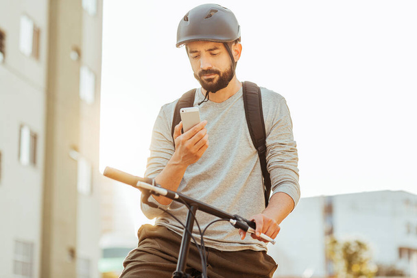 Cyclist standing looking at his smartphone in the city. Concept of using gps map or delivery apps - Foto, Imagem