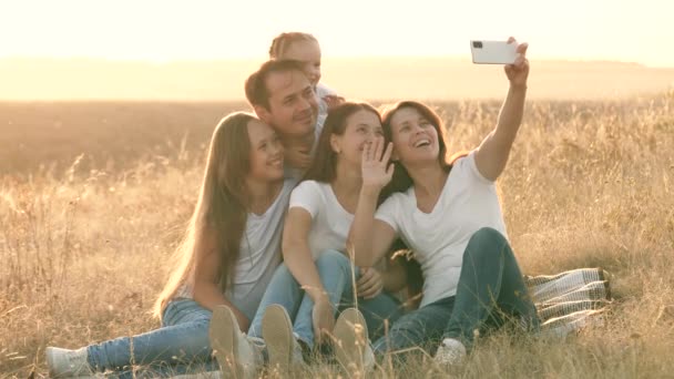 glückliche Familienreisen. Selfie mit dem Smartphone im Park. Mama, Papa und Kinder sitzen auf einer Decke und filmen ein Video. Mutter und Vater mit ihren Töchtern werden vor Ort fotografiert. Familie von Bloggern - Filmmaterial, Video