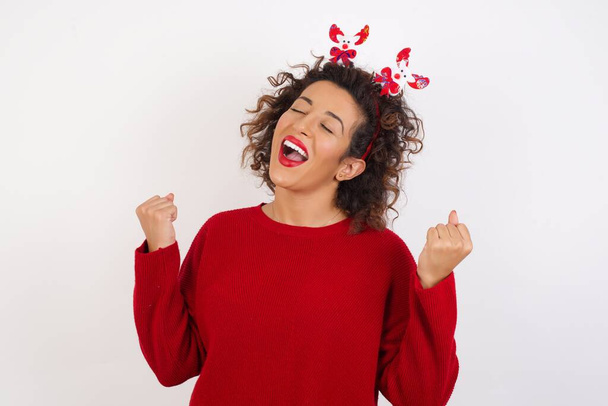 Young woman wearing deer horns headband, celebrating surprised and amazed for success with arms raised and eyes closed. Winner concept - Фото, изображение
