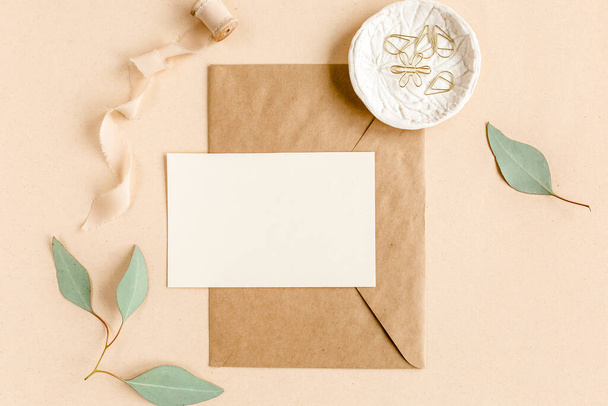 Mockup invitation, blank greeting card and craft envelope, green leaves eucalyptus. Flat lay, top view. - Foto, afbeelding