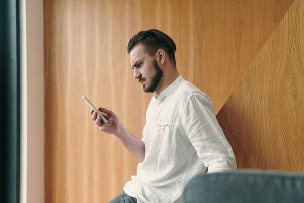 Porträt eines fokussierten jungen Geschäftsmanns, der sein Smartphone in der Hand hält und auf den Bildschirm blickt - Foto, Bild