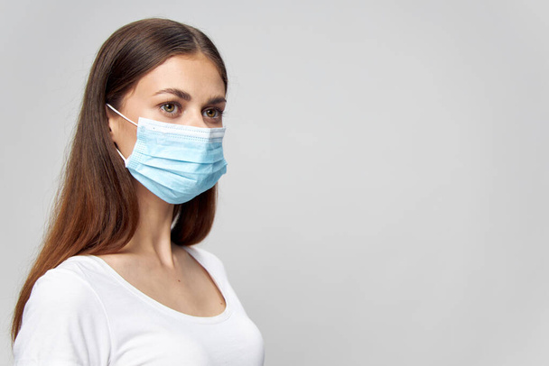 Woman in a white T-shirt and in a medical mask on an isolated background - Fotó, kép