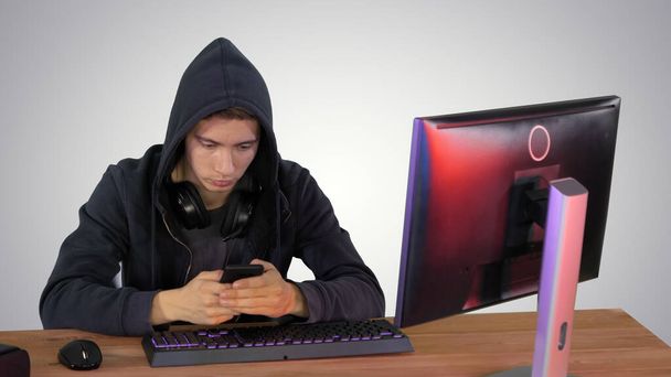 Hacker s kapucí pomocí notebooku a smartphonu na pozadí přechodu - Fotografie, Obrázek