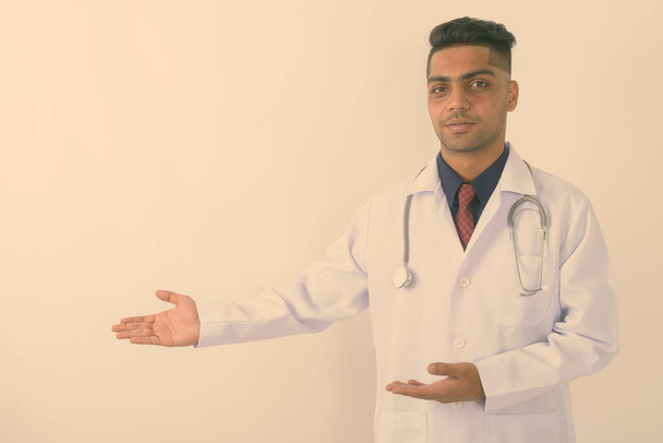 Studio shot of young Indian man doctor showing something against white background - Foto, afbeelding