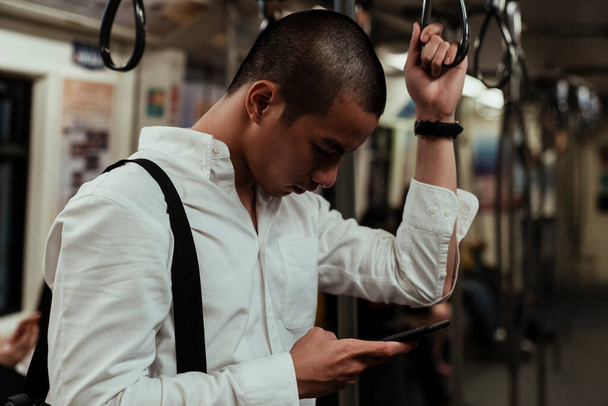 Un hombre revisando su teléfono mientras toma un skytrain para volver a casa una vez que termine su trabajo. - Foto, Imagen