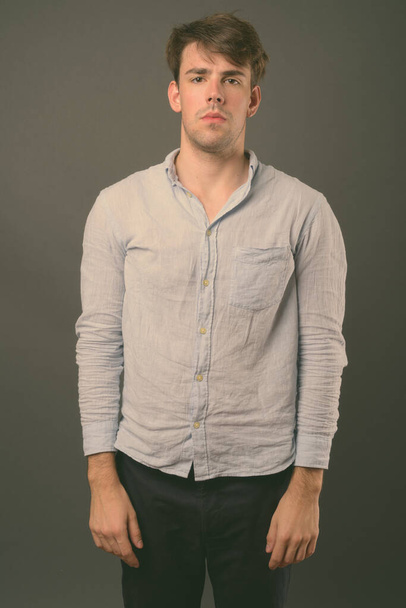 Studio shot of young handsome man wearing blue shirt against gray background - Foto, Imagem
