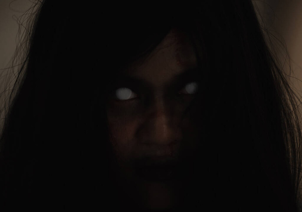Girl zombie in blood. Closeup face and eyes of Asian Woman ghost with blood. Horror creepy scary fear in a dark house. Hair covering the face, Halloween festival concept - Foto, Imagen