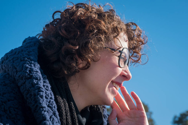 Jeune femme aux cheveux bouclés portant des lunettes avec sa main sur son visage. - Photo, image