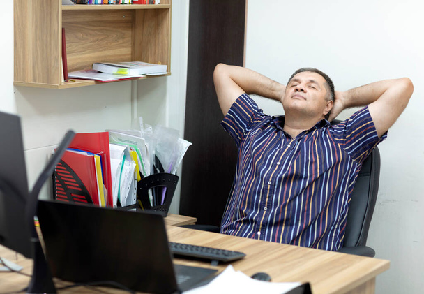 Um homem está descansando no escritório, inclinando-se para trás em sua cadeira. - Foto, Imagem