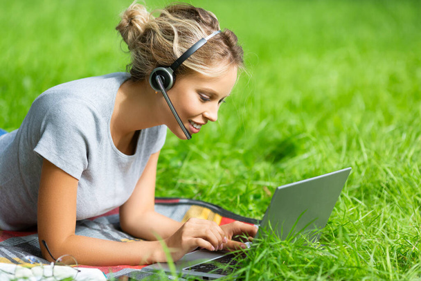 Mladá žena - sledování vzdělávacího webináře na notebooku, ležící na zelené trávě. - Fotografie, Obrázek