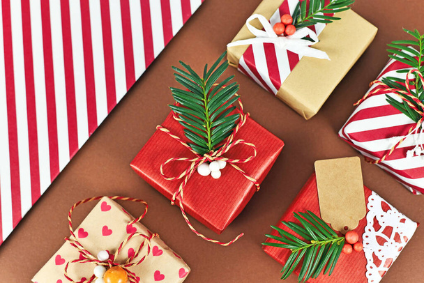 Top view of beautiful red, white and natural brown decorated Christmas gift boxes with ribbons and fir branches on brown background - Fotó, kép