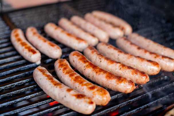 Sausages on grill, with smoke above it.Pork sausages grilling on a portable BBQ with one sausage being turned in a pair of tongs on a summer picnic, close up of the grill, meat and fire - 写真・画像