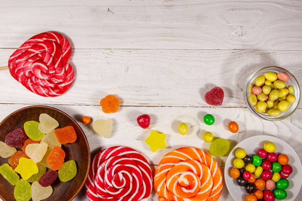 Coloridos caramelos de chocolate, piruletas y dulces de gelatina en la mesa de madera blanca - Foto, Imagen