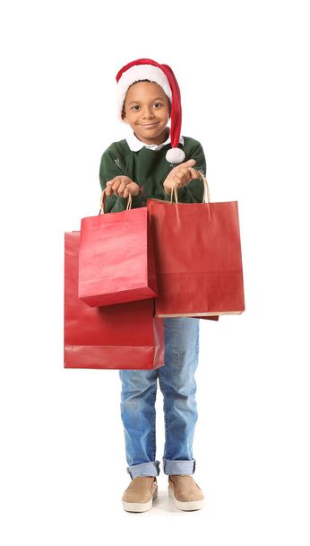 Cute African-American boy in Santa hat and with shopping bags on white background - Фото, зображення
