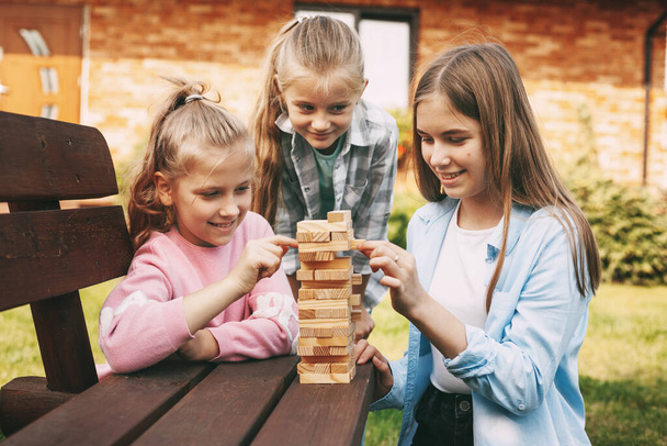 Τρεις φίλες παίζουν ένα ξύλινο επιτραπέζιο παιχνίδι έξω κοντά στο σπίτι τους. - Φωτογραφία, εικόνα