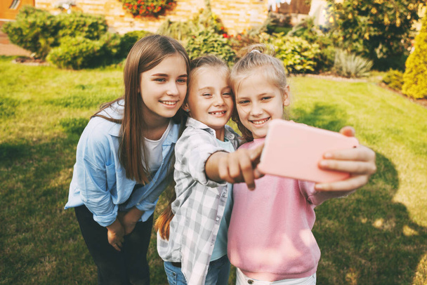 幸せな十代の女の子のグループが笑って、屋外の携帯電話で自撮り. - 写真・画像