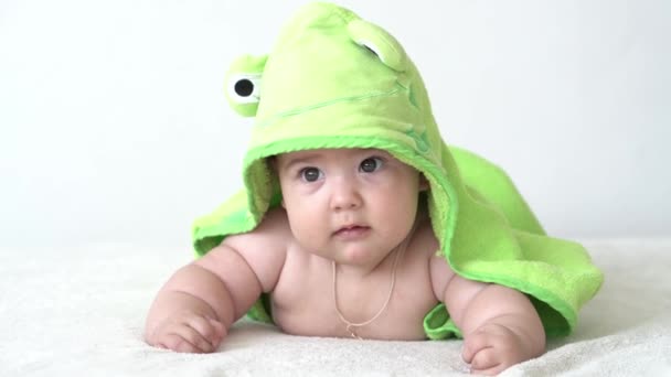 Çocukluk, günlük rutin, hijyen bebek konseptleri - yakın plan mutlu çocuk beyaz arka planda yeşil kurbağa havlusu. Bebek duştan sonra karın üstü yatar. bebek uyanma zamanı - Video, Çekim