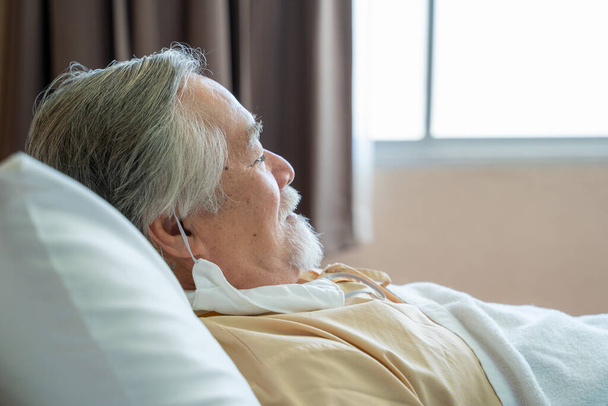 Paciente mayor descansa acostado en la cama en el hospital. - Foto, Imagen