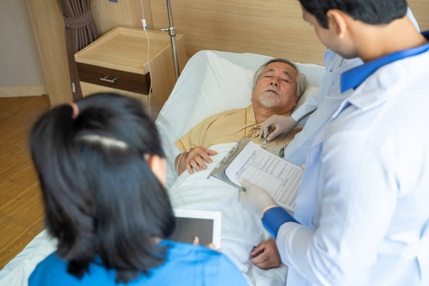 Equipo médico En rondas que se reúnen alrededor de la cama del paciente masculino mayor en el hospital, los médicos discuten el informe en el portapapeles. - Foto, imagen