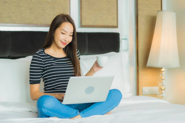 Portré gyönyörű fiatal ázsiai nő használ számítógép laptop az ágyban a hálószoba belső - Fotó, kép