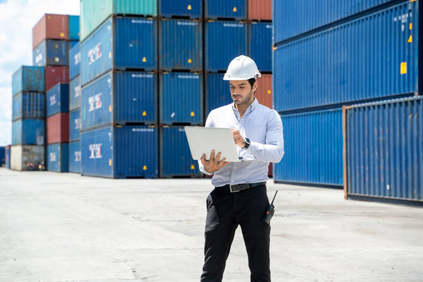 Businessman standing and using walkie talkie checking stock into container for loading in shipping port. - Photo, Image