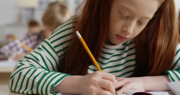 Közelkép a kaukázusi tini aranyos vörös hajú iskolás lány írásban a copybook egy gyakorlat a lecke vizsga az iskolában. - Felvétel, videó