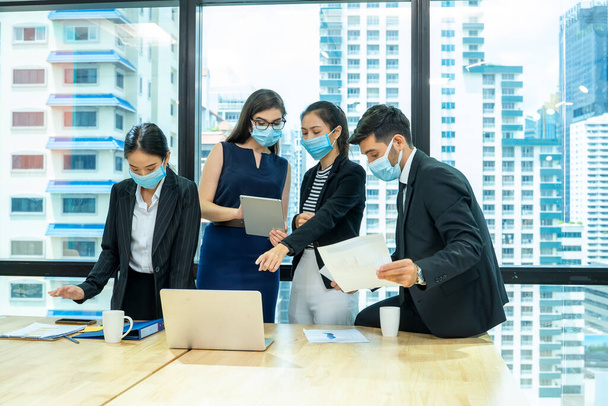 Mitarbeiter der Gruppe mit medizinischer Gesichtsmaske, die als sozialdistanzierende Maßnahme im Geschäftsbüro arbeitet, während neue normale Veränderungen nach Coronavirus oder Pandemie nach Covid-19-Ausbruch stattfinden. - Foto, Bild