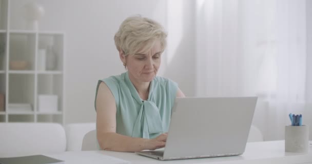 vrouw van middelbare leeftijd werkt met laptop voelt hoofdpijn, raakt het voorhoofd door handen, oververmoeidheid en vermoeidheid - Video