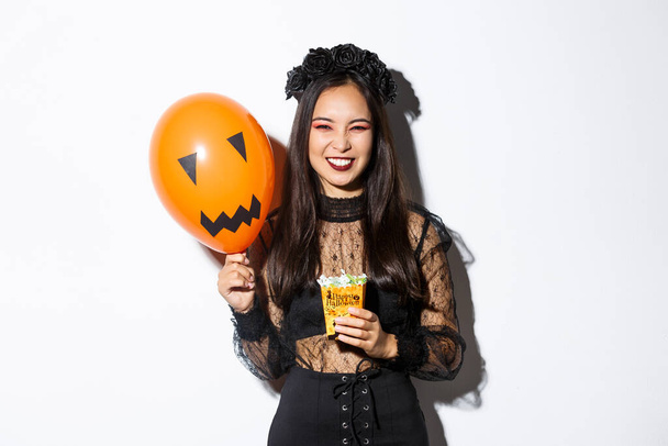 sassy belle asiatique femme appréciant astuce ou traiter, célébrer halloween, tenant orange ballon et bonbons - Photo, image