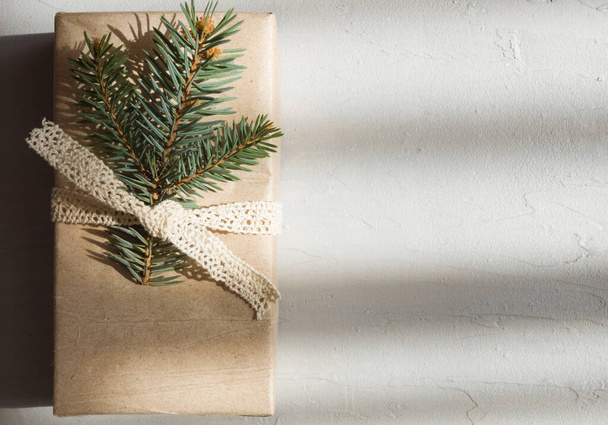 Ένα ορθογώνιο κουτί σε χάρτινη συσκευασία είναι διακοσμημένο με ένα κλαδί ερυθρελάτης. Χριστουγεννιάτικο δώρο σε μινιμαλιστικό στυλ σε τσιμεντένιο φόντο. - Φωτογραφία, εικόνα