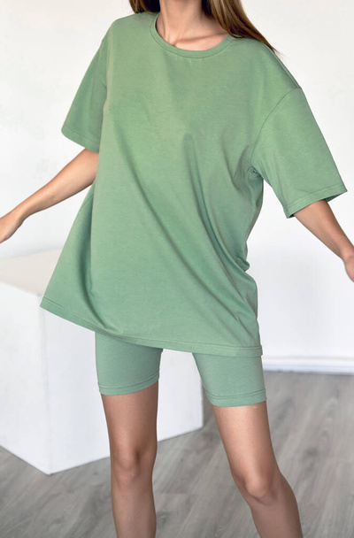 Frau trägt grünes Oversize-T-Shirt mit Kopierraum. Indoor Studio Kleidung Attrappe - Foto, Bild