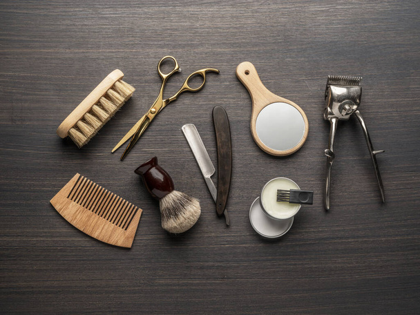Klassische Pflege- und Friseurwerkzeuge auf Holzgrund. Draufsicht auf Barbershop-Instrumente, die auf dunklem Holztisch liegen. - Foto, Bild