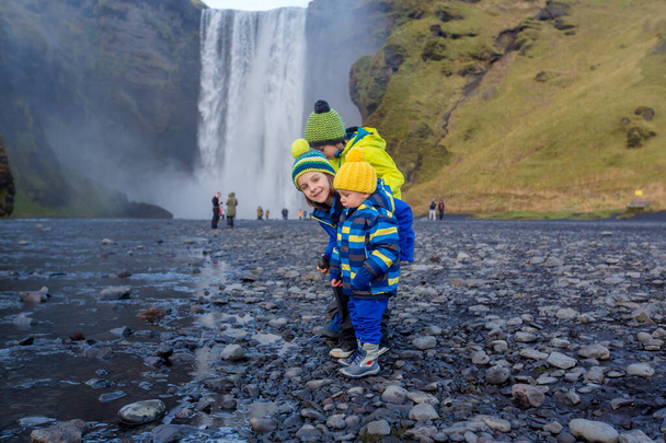 Cute child playing in front of the Skogafoss waterfall in Iceland on a sunset cloudy day, autumntime - Foto, imagen