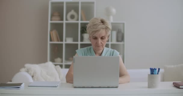 Orta yaşlı bir kadın evde dizüstü bilgisayarla çalışıyor, internet sitelerine bakıyor ve sosyal ağlarda iletişim kuruyor. - Video, Çekim